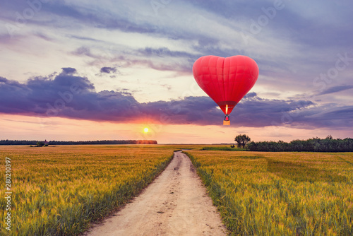 Red hot air balloon in the shape of a heart above the field.