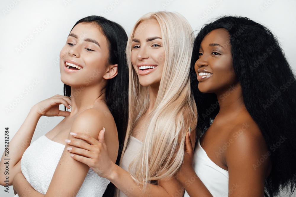 Beauty photo of three smiling multiracial women with different types of skin: Caucasian, African american and Asian girls, isolated over white background. Beautiful young women with natural make-up. Beauty photo of three smiling multiracial women with different types of skin: Caucasian, African american and Asian girls, isolated over white background. Beautiful young women with natural make-up.