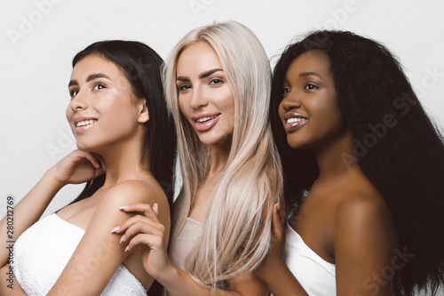 Beauty photo of three smiling multiracial women with different types of skin: Caucasian, African american and Asian girls, isolated over white background. Beautiful young women with natural make-up.