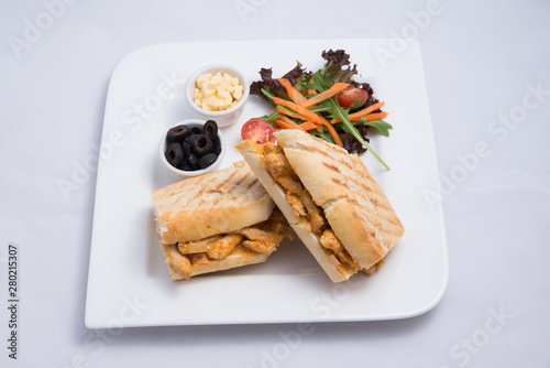 A low contrast Hero shot of a breakfast platter with grilled chicken panini sandwich with olives, cheese & vegetables on a minimal white background with a 45 degree angle from almost front perspective
