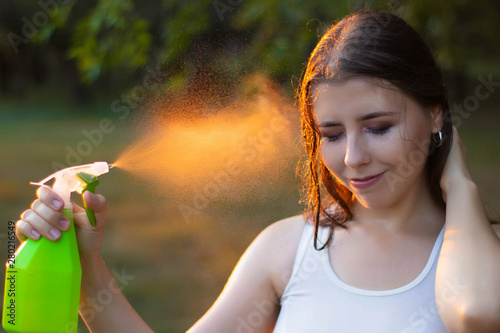 Young woman spraying water on herself from a spray bottle, close-up. Summer heat, sunset © Elena