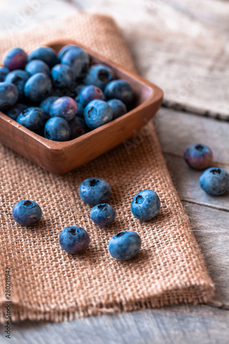 Blueberries in a wood bowl on top of burlap with a wooden table top