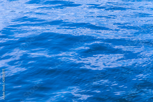 The background or texture of the blue water surface of the river, lake or sea with the waves, ripples and flares
