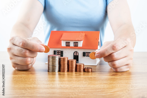 Housewife saves money to buy a house, female hand takes coins and small house model on the desktop