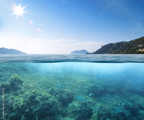 Blue sunny sky, an island in the ocean and underwater sandy rocky sea view. © magdal3na