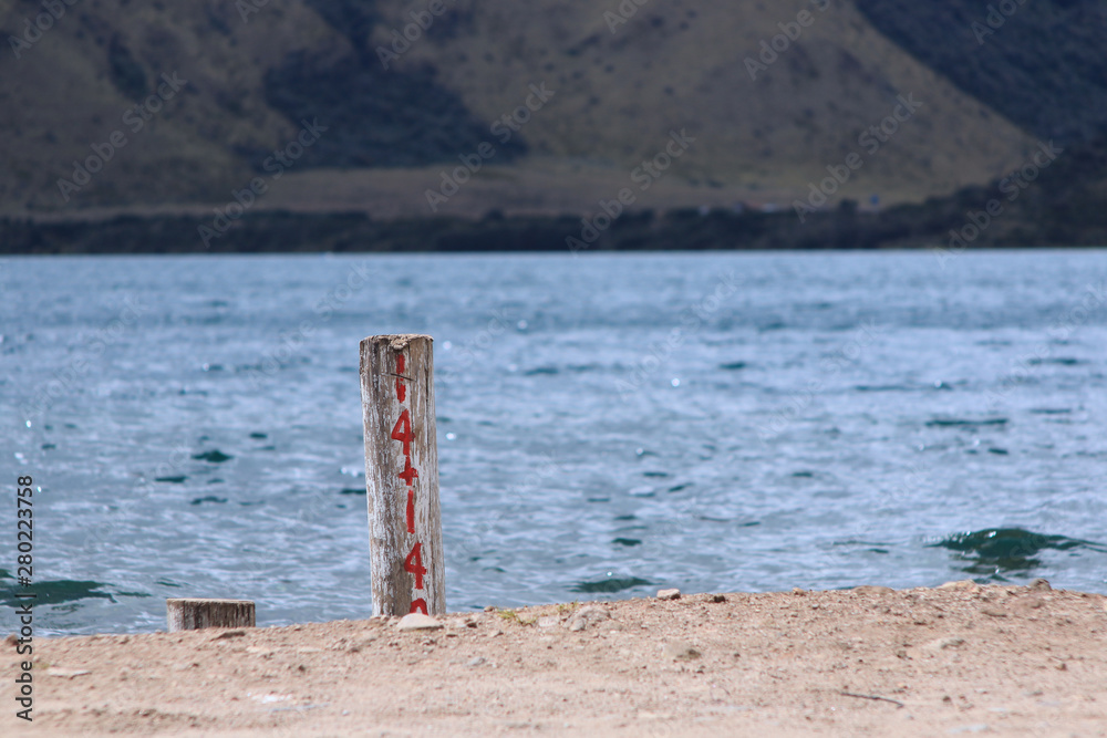 A pole with a number written in red next to the water with mountains in the background