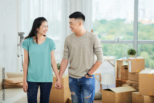 Happy Asian couple standing holding hands and smiling to each other while moving to the new house