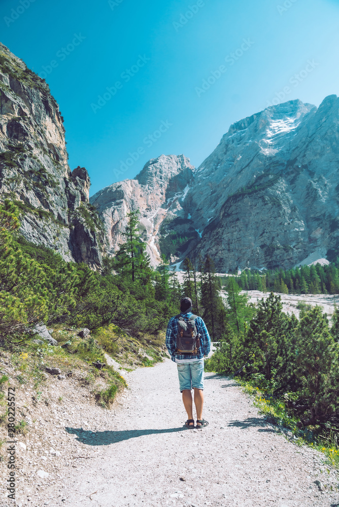 Naklejka premium young man with backpack walking by mountains trail in sunny day