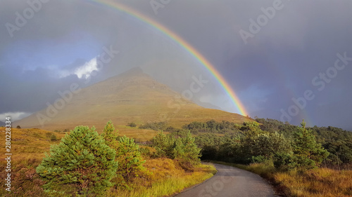 beautiful rainbow in dramatic sky over a road crossing colorful land