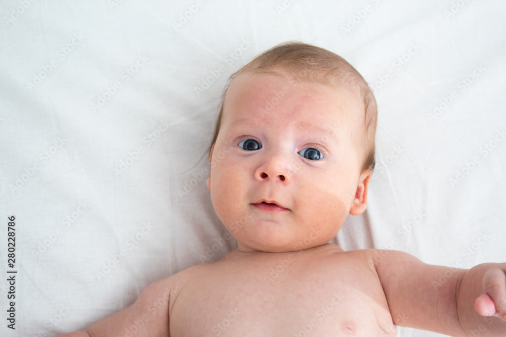 The baby a surprised expression. Newborn lying on a white background .Top view The baby a surprised expression. Newborn lying on a white background .Top view
