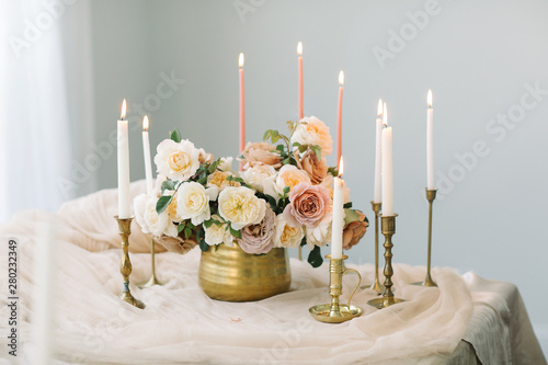 Flowers in golden vase with candles in vintage brass candle holders on the table