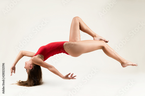 A beautiful long-haired long-legged slim girl wearing a red body levitates on a white background, touching the floor only with her hair. Advertising, conceptual, art and commercial design. Copy space.