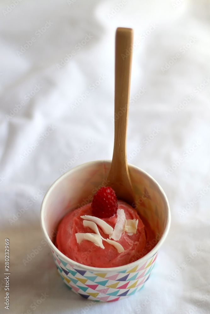 Fototapeta premium Strawberry vegan ice cream, decorated with raspberry and coconut flakes, in colorful paper cup. Selective focus.