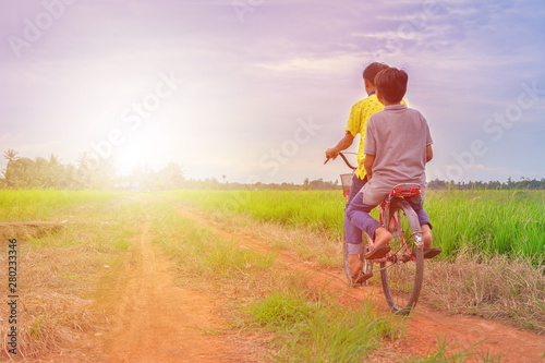 Fototapeta Naklejka Na Ścianę i Meble -  happy young local boy riding old bicycle at paddy field with sunlight