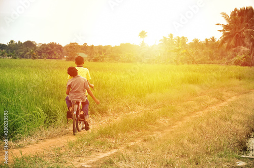 happy young local boy riding old bicycle at paddy field with sunlight