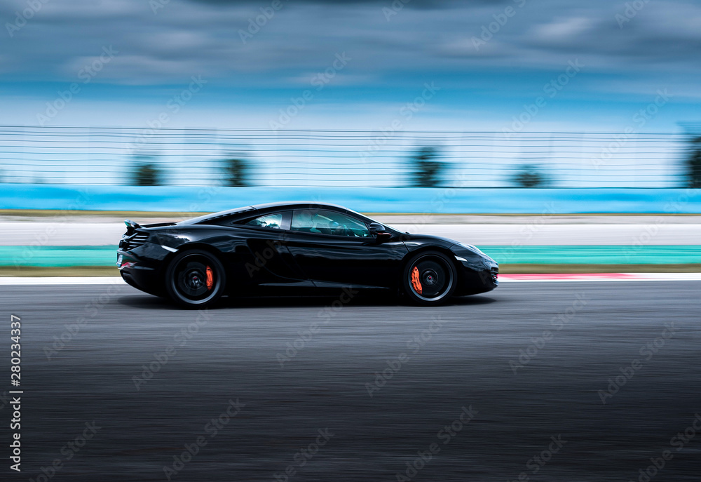 Black cabriolet sport sedan car side view driving on the highway, nature background. 