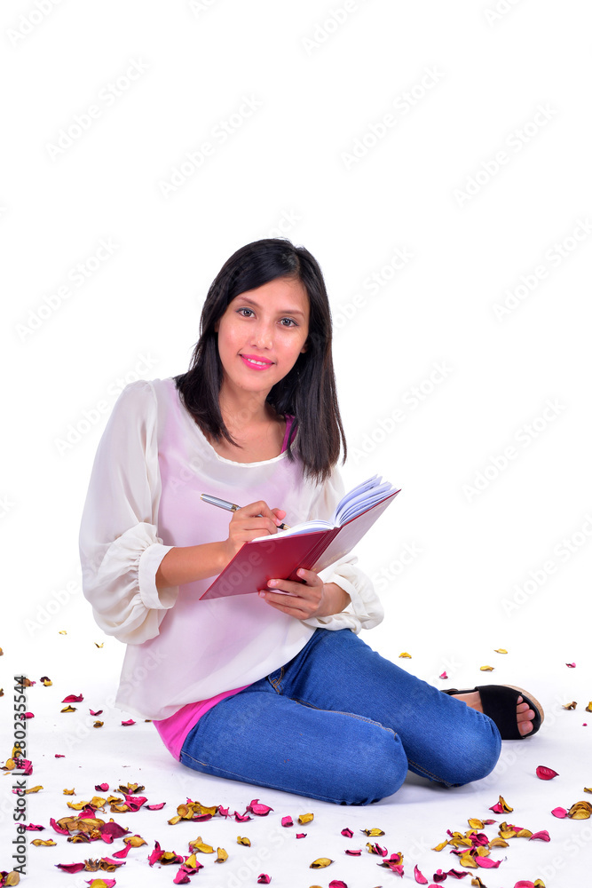 Beautiful woman sitting on the white floor while writing a letter surrounded by rose petals Beautiful woman sitting on the white floor while writing a letter surrounded by rose petals