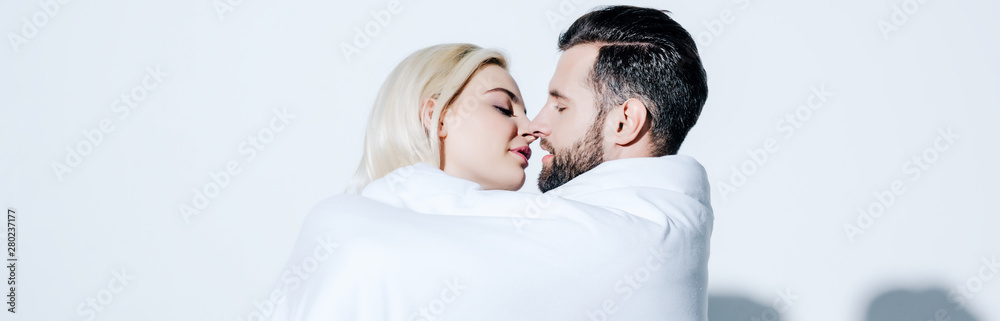 panoramic shot of girlfriend and boyfriend covered in blanket ready for kissing on white