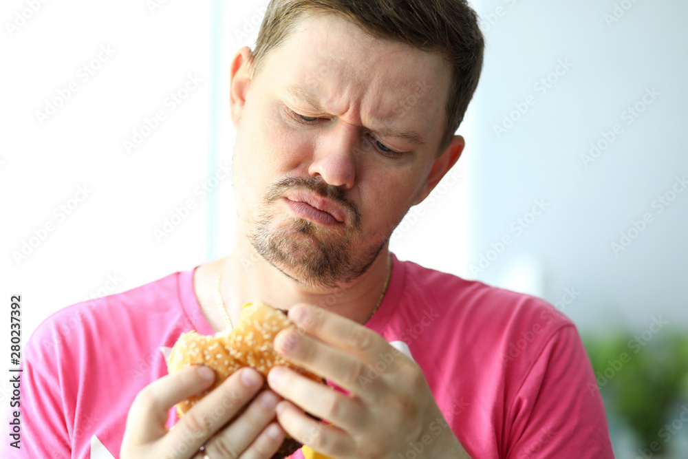 Unhappy bearded man looking at burger with suspicious Unhappy bearded man looking at burger with suspicious