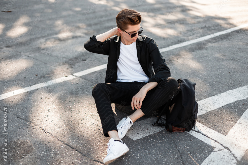 Nice young hipster in elegant black clothes in white sneakers with a backpack