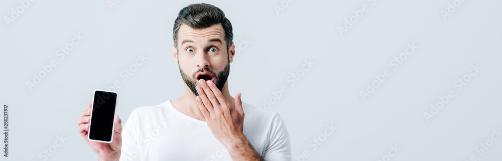 panoramic shot of shocked man showing smartphone with blank screen isolated on grey panoramic shot of shocked man showing smartphone with blank screen isolated on grey
