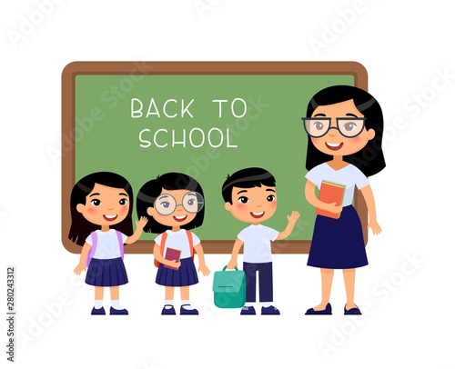 Teacher greeting pupils in classroom flat vector illustration. Boys and girls dressed in school uniform and female teacher pointing at blackboard cartoon characters. Primary students back to school