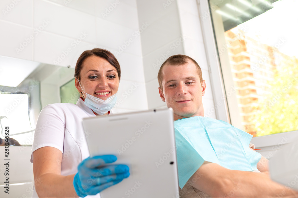 Obraz premium Dentist finishing successful teeth restoration, black haired doctor, in green mask, giving to happy patient mirror, beautiful long-haired woman looking at pristine white teeth with great pleasure