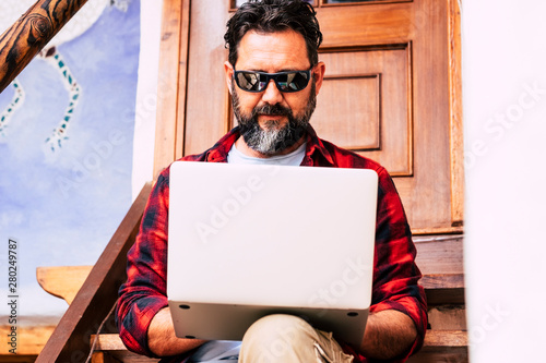 Hipster adult man with beard use personal laptop computer outdoor home sit down on a stairs - internet connection everywhere concept with people and technology use - alternativer office photo