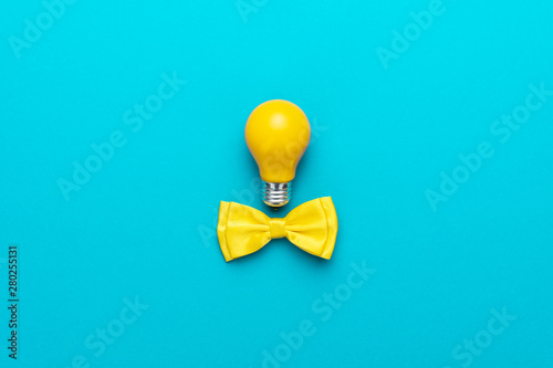 Top view photo of smart idea with yellow bulb and bow tie. Minimalist flat lay image of bow tie and lightbulb over turquoise blue background with copy space. Central composition of great idea concept.