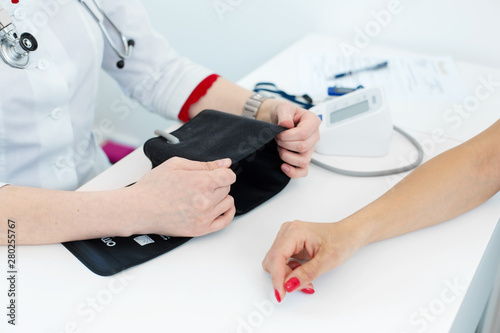 Professional female doctor putting on device for measuring pressure on young female patient hand in hospital room