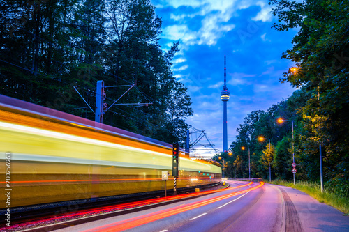 Obraz na płótnie Germany, Illuminated tramway passing by street of traffic next to television tower of stuttgart city in green forest nature landscape in magical twilight mood after sunset w salonie
