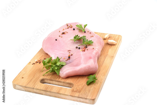 Raw turkey fillet with parsley and  spices on a wooden cutting board over white background.