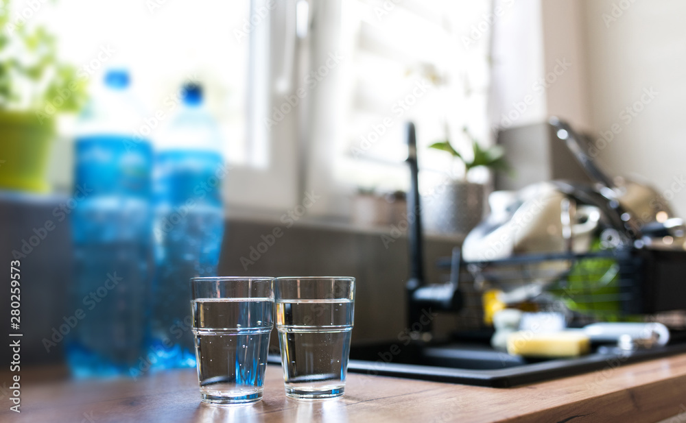 Two glasses of water in kitchen, with tap water and two bottles of mineral water. Shallow depth of field. Water shortage concept, saving water. Body hydration with clean & clear water.