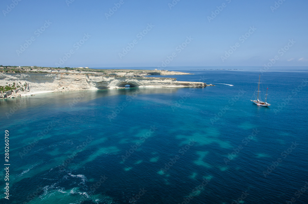 Boat in Mediterranean Sea with blue water and white rocks in Malta near Marsaxlokk, Saint Peter Pool.