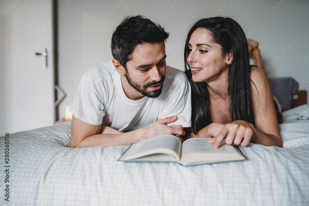 Loving couple reading a book in bed at home in a moment of relax Loving couple reading a book in bed at home in a moment of relax