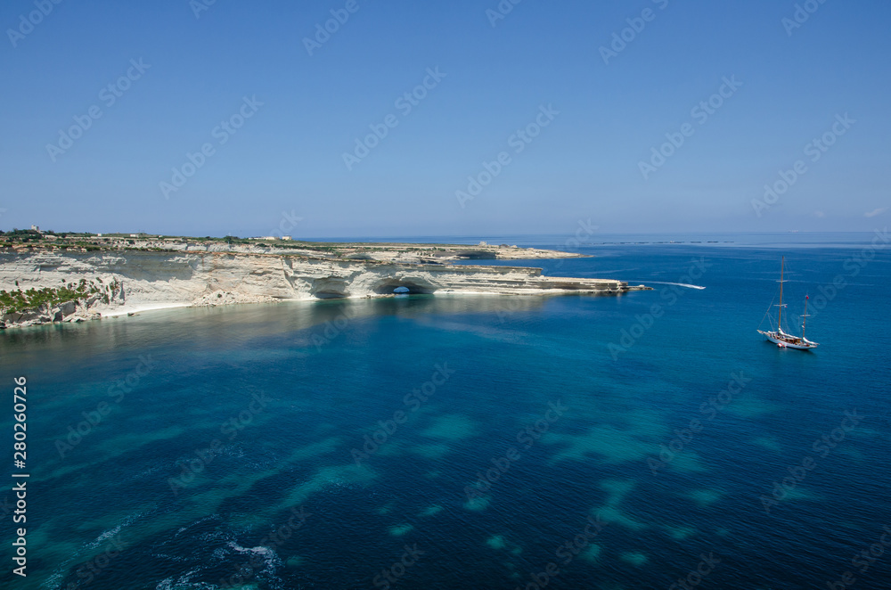 Boat with landscape with Mediterranean Sea with blue water and white rocks in Malta near Marsaxlokk, Saint Peter Pool.