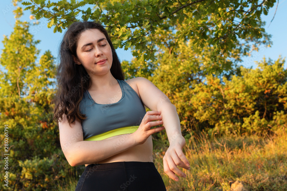 A young athletic woman scratches her hand from an insect bite during training. The concept of protection from insect bites and outdoor recreation. Close up A young athletic woman scratches her hand from an insect bite during training. The concept of protection from insect bites and outdoor recreation. Close up