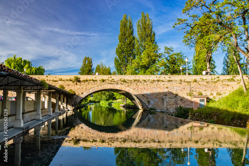 The ancient wash-house and the masonry bridge over the river, in the medieval village of Bevagna. Perugia, Umbria, Italy. Blue sky at sunset. Trees and vegetation. The reflection on the water surface.