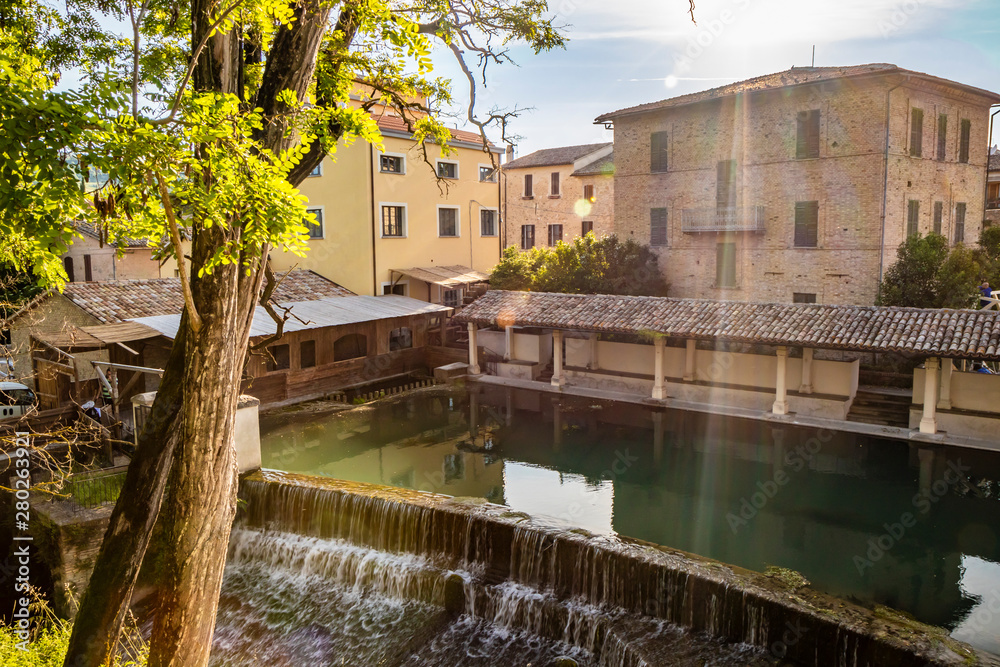 The ancient wooden wash house, on the river, in the medieval village of Bevagna. Umbria, Italy. The blue sky at sunset. Trees and vegetation. The reflection of the buildings on the water surface.