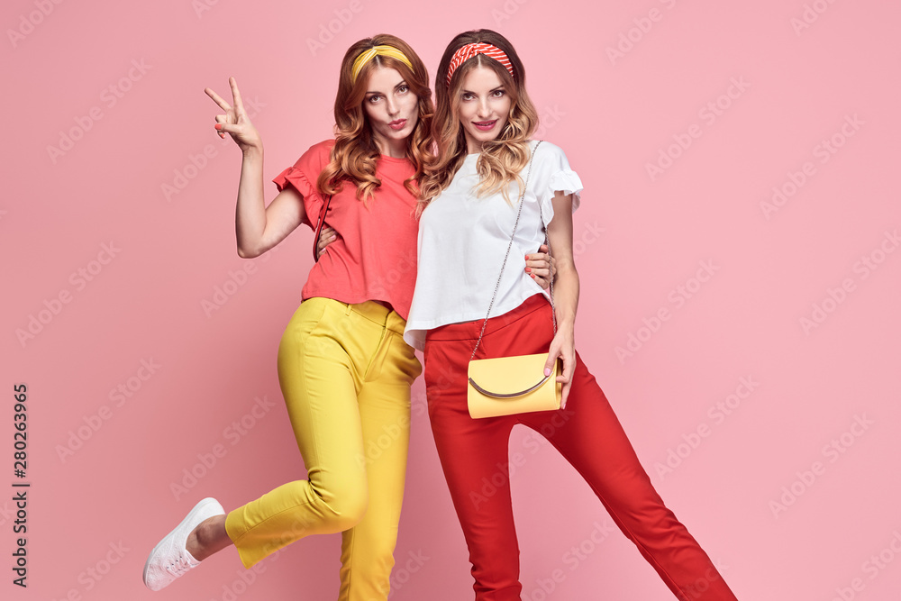 Fashionable embracing woman sisters smiling on pink background. Two Shapely Girl Having Fun dance, Trendy yellow coral summer outfit, fashion hairstyle, makeup. Gorgeous female model, funny concept Fashionable embracing woman sisters smiling on pink background. Two Shapely Girl Having Fun dance, Trendy yellow coral summer outfit, fashion hairstyle, makeup. Gorgeous female model, funny concept