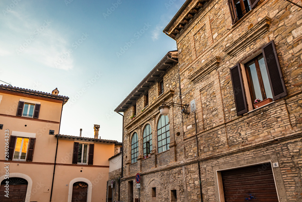 The ancient stone and brick buildings of the medieval village of Bevagna. New buildings plastered and painted. Perugia, Umbria, Italy. The church bell tower at the bottom. The blue sky at sunset.
