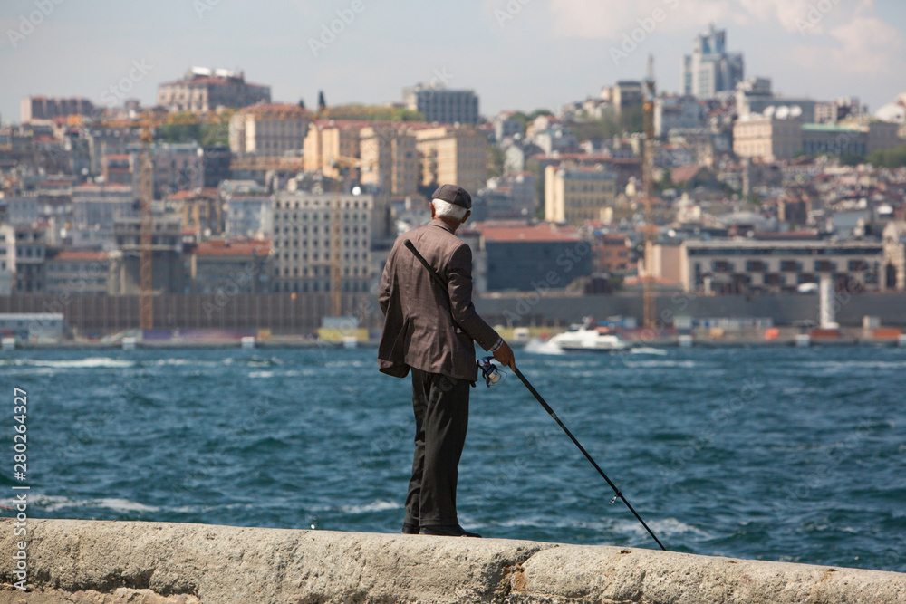 Turkey, Istanbul. Old fisherman with a fishing rod on the coast. the background of the cityscape.  fishing in the Bosphorus