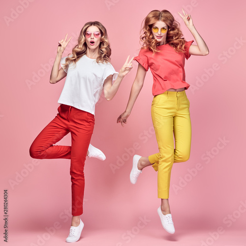Fashion. Two Inspired woman laughing dance. Excited joyful friend Having Fun, Stylish fashionable summer outfit. Carefree Girl friends with curly hair jump dancing in Studio, happy positive emotion