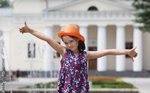 Little girl in a straw hat on the background of the fountain