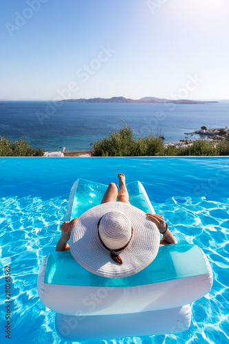 Sommerurlaubs Konzept: Unbekannte Frau mit weißem Hut entspannt in einem Pool auf einer Luftmatratze und genießt die Aussicht auf das Meer