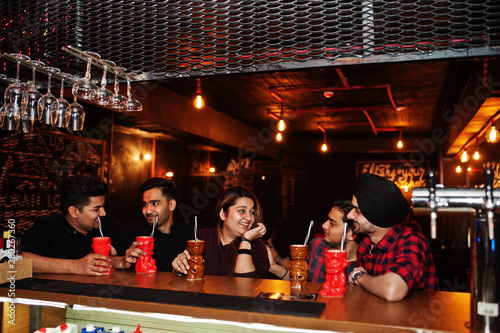  Group of indian friends having fun and rest at night club, drinking cocktails near bar counter.