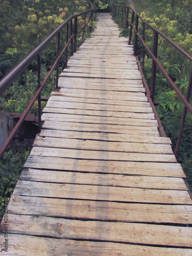 Old rustic bridge of wooden planks on a metal base with iron handrails, going into perspective.