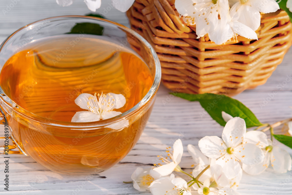 Basket with Flowers of philadelphus somewhere called jasmine or mock orange and Cup with fragrant jasmine tea on a white wooden tray outdoors in summer