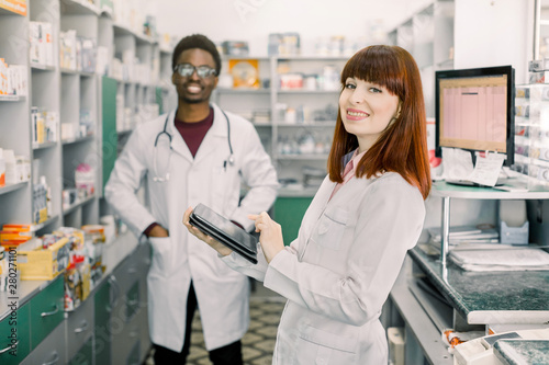 Portrait of a multiethnical male and female pharmacists smiling in front of medicines at drugstore