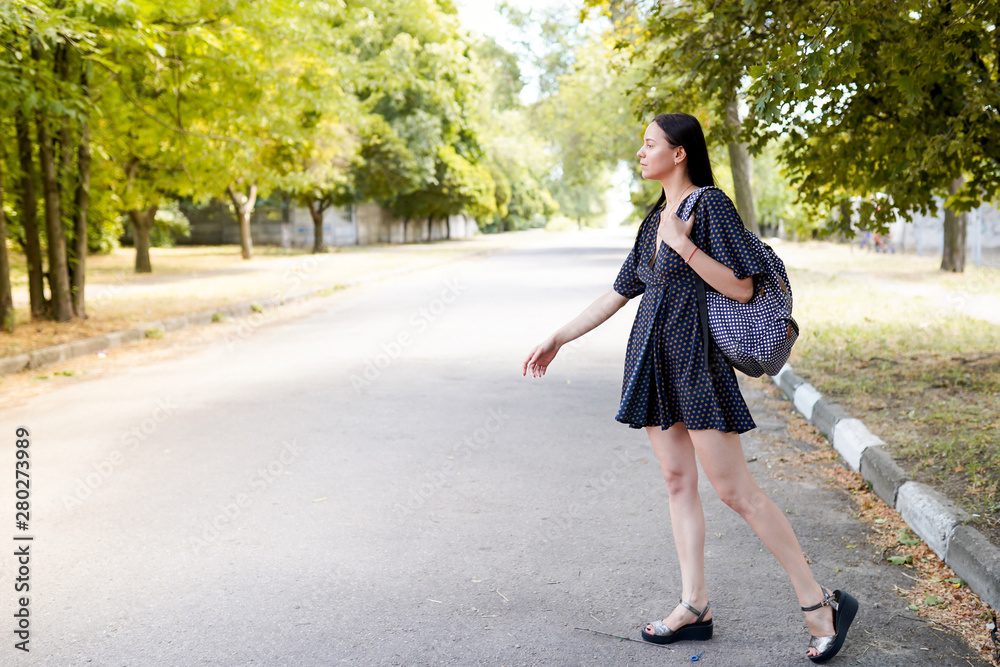 Traveler woman looks away on road. girl in dress and bag, nature background with copy space